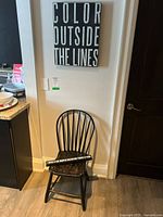 Photo of a black painted wooden chair under a wall sign, chair shows wear consistent with used furniture.