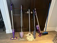 Full view of all cleaning tools including steam mops, mop, broom, and electric cleaner