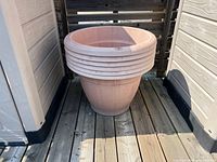 Front angled view of large light beige flower pot with horizontal ridges on wide rim, placed on wooden deck.