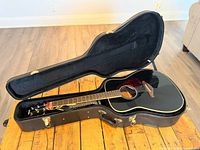 Open hardshell case displaying black acoustic guitar inside