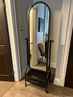 Full angled view of tall hallway mirror with metal frame and drawer on the bottom, positioned on casters.