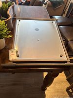 Back side of rectangular glass mirror showing mounting points and a metallic copper tubular frame resting on a wood table