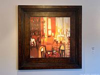 Framed metal print artwork hanging on a wall showing a warm dining room scene in a dark textured metal frame.