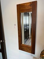 Front angled view of the rectangular wooden frame mirror mounted on the wall showing wood grain details and reflection of doorway.
