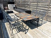 Photo shows the full patio set on a wooden deck with four metal chairs and rectangular table featuring tile inlay tabletop.
