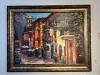 Full view of the large framed painting print showing a Mediterranean village scene with buildings, flowers and a tower in the background.
