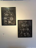 Two framed prints hanging on a wall, one with two bicycle patent drawings and the other with a motorcycle patent drawing