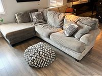 Gray sectional sectional couch with a chaise lounge and matching ottoman on wood flooring, with two decorative pillows featuring spiral patterns.