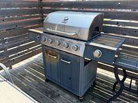 Front side view of Giantex propane gas grill with five burner knobs, side burner on right, two-door cabinet below, on a rooftop patio.