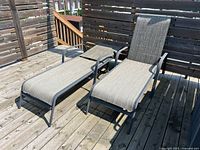 Two matching adjustable patio lounge chairs on a wooden deck, showing front angle with armrests and fabric seats.