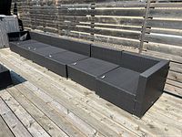 Long outdoor patio sectional arranged in one continuous row against a wooden fence on a deck, showing the entire length and woven rattan texture.