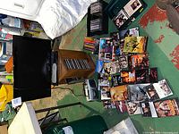 Full lot overview with Toshiba TV, remote and stand, media collection including DVDs, CDs, VHS tapes, Venturer cassette radio, and wooden CD stand on floor.