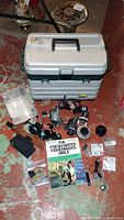 Front-facing photo of the entire fishing gear lot showing the tackle box, reels, rod, tackle containers, and guidebook on a concrete floor.