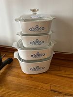 Four CorningWare casserole dishes stacked by size with lids, showing Cornflower Blue pattern.