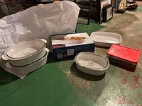 Photo of CorningWare French White bakeware set including three oval ceramic casserole dishes with glass lids, a rectangular white ceramic dish, a rectangular glass storage container with red lid, and packaging box.