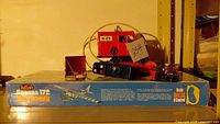 Photo showing the Guillow's Cessna 172 Skyhawk model kit box with visible branding and text, along with the red Cragstan crane toy and its magnetic shovel attachment placed on top.
