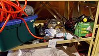 Shelf with digital air compressor, two flashlights, assorted light bulbs including a green box of Luminous halogen bulbs, and an orange extension cord in a plastic bin.