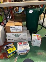 Overall view of the green Orbis trash bin and the stack of boxes containing various brands and types of garbage bags