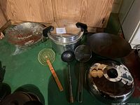 Photo of lot including large pressure cooker, steel colander, seasoned wok, stainless steel steamer basket, and three cooking utensils.