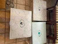 Three large white/light pastel boxes labeled with brand logos from bedspread/coverlet brands stacked on floor.