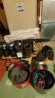 Overview of men's footwear including Birkenstock sandals size 42, gloves, hats stored in tins, folded fabric item, and umbrella on the floor against a beige appliance.
