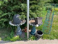 Wide view showing two concrete bird baths, a dome cover, square planters, and tomato cages