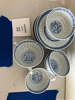 Top view of 3 white porcelain rice bowls and 3 matching cups with saucers, all featuring blue dragon motifs and geometric border patterns. Lot tag visible next to items.