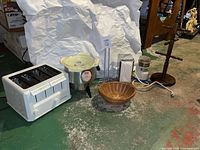 Photo showing white Proctor-Silex 4-slice toaster, Chilton electric corn popper with glass bowl, napkin dispenser, wooden bowl, electric coffee grinder with cord, and wooden mug rack arranged on a green floor.