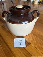Robinson Ransbottom stoneware crock with lid on hardwood floor, showcasing brown and cream two-tone color and shape with twin handles.