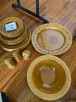 Stack of plates and bowls with embossed grape and vine border, salt and pepper shakers in matching mustard yellow glaze.