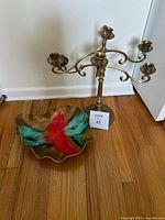 Brass candelabra standing next to a hand-painted glass bowl on a wooden floor against a white wall.