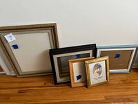 Five picture frames assorted in sizes and colors seen against a white wall and wood floor