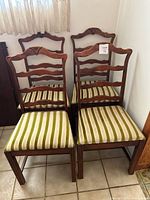 Front view showing four solid wood dining chairs with carved backs and green and white striped cushions.