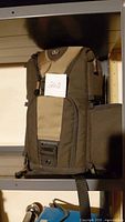 Photo of brown and beige camera sling/shoulder bag with multiple compartments and clips, displayed on shelf.