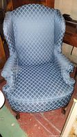 Full front view of wingback armchair showing blue diamond pattern upholstery and wooden legs.