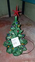 Front view of the ceramic Christmas tree with multicolor bulbs and red star topper on a concrete floor, showing the overall shape and condition.