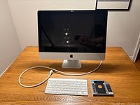 Front view of Apple iMac with keyboard, power cord, and SATA adapter on table