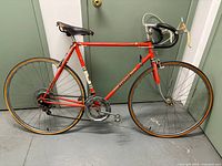 Full left side view of orange Peugeot road bicycle with drop bars