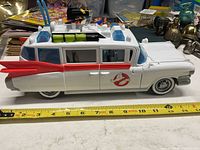 Side view of white Ghostbusters Ecto-1 diecast model car showing red stripe, Ghostbusters logo, and rooftop ghost-catching equipment.