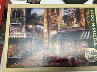 Top of the puzzle box showing the full image of the completed puzzle with Italian street scene and cafe, labeled 'Buon Appetito' with 1000 pieces