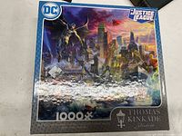 Box of the 1000-piece Justice League puzzle with artwork showing superheroes over cityscape, branded by Thomas Kinkade Studios.