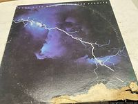 Front cover of Dire Straits Love Over Gold vinyl LP showing lightning bolt design with visible wear and damage on bottom edge.