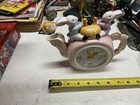 Front view of porcelain teapot clock with bunnies and honey pot, showing clock face and bunny figurines.