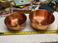 Two copper pots of different sizes placed next to a measuring tape showing their diameters.