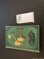 Front cover of green gilt-decorated book alongside size reference slip