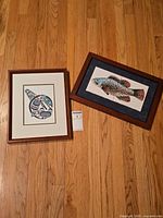 Both framed artworks on hardwood floor: whale print left, fish tile art right
