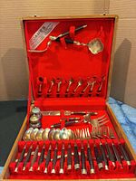 Open wooden case showing full set of flatware, serving pieces and red interior