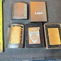 Overview of three Zippo lighters with two branded boxes and one tin, measuring tape for scale