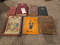 Seven hardcover books arranged on carpet showing covers and spines