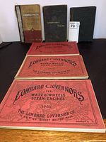 Front view of all six catalogs—three red Lombard Governor catalogs in foreground, Logarithmic Tables, Hawkins Electric, and Cloughson Twist Drill Co. volumes in back